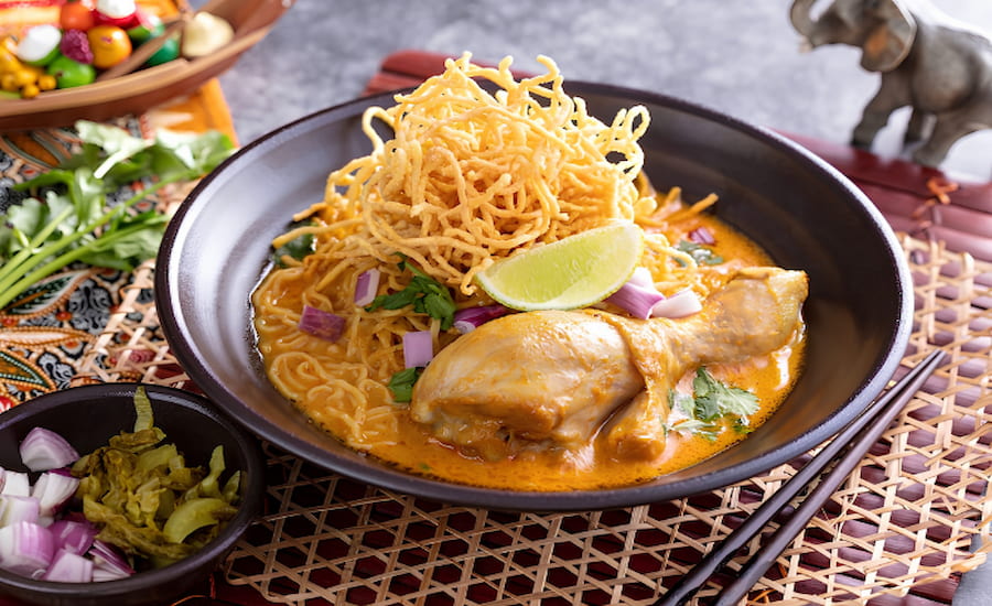 Una deliziosa ciotola di Khao Soi fumante guarnita con noodles croccanti e lime